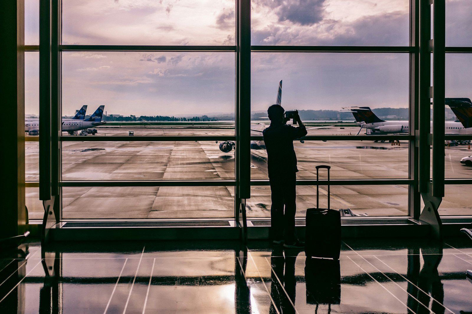 Traveler with suitcase watching planes at an airport window at dusk